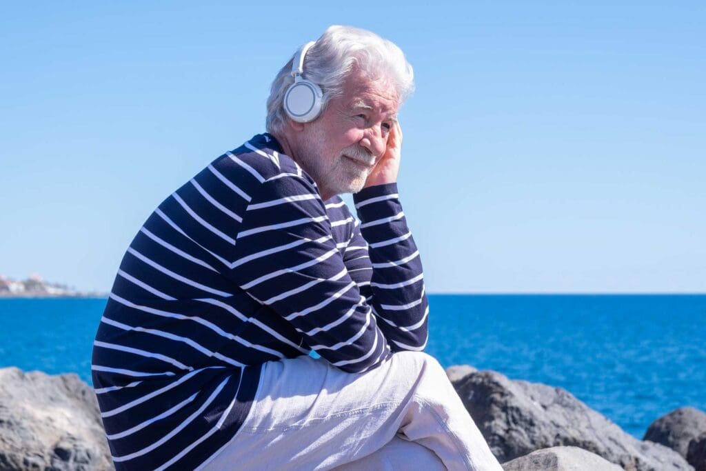 Senior Man Listening to Music with Headphones at the Beach